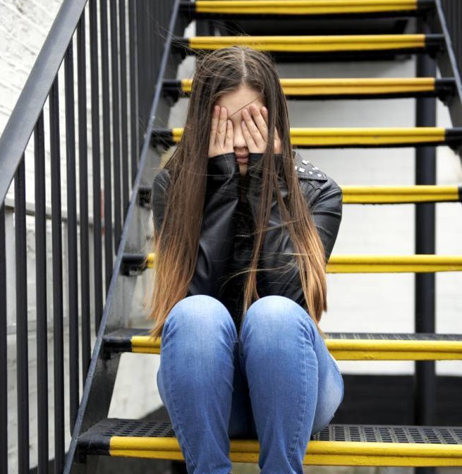 Girl sitting on stairs with her hads over her eyes.